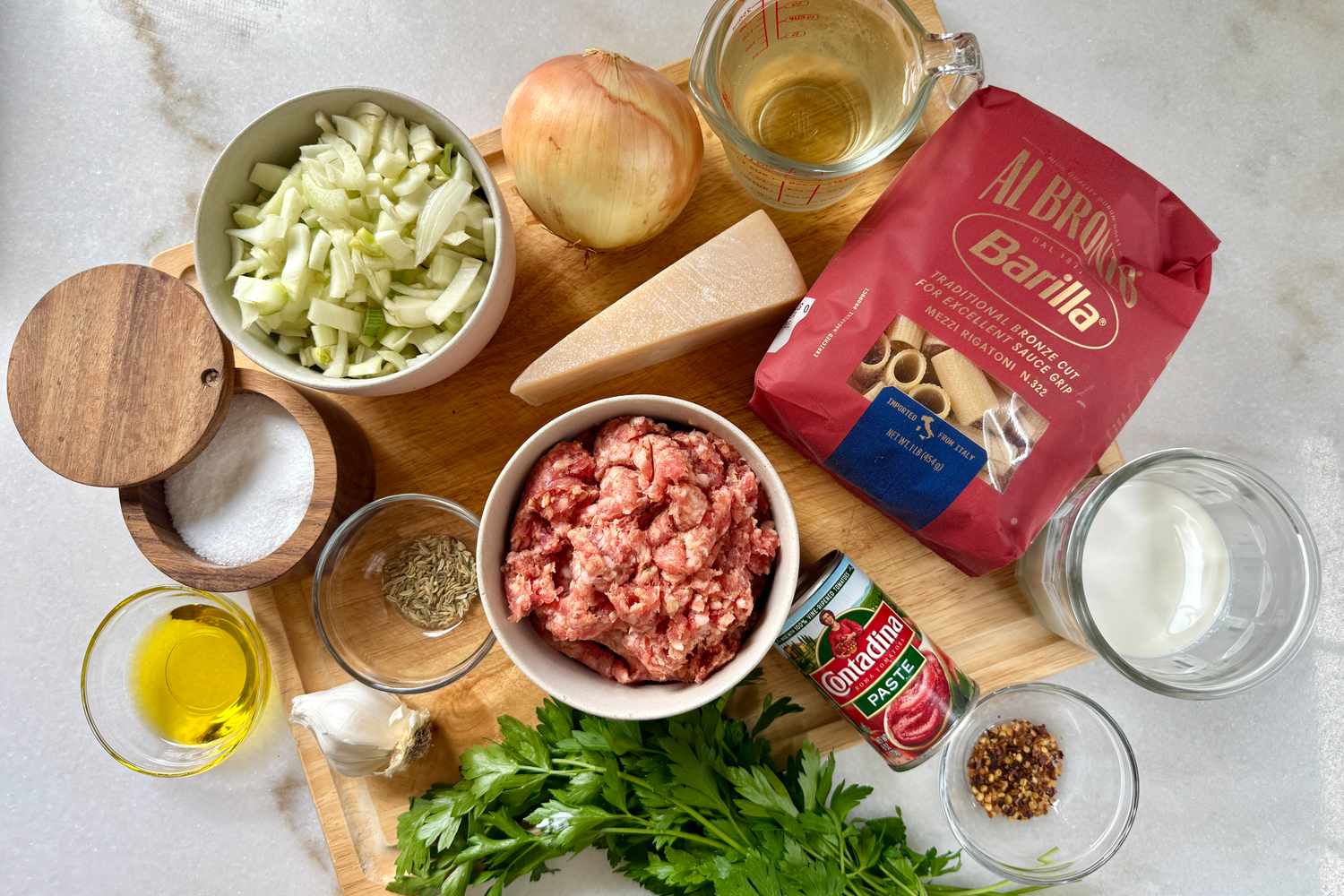 Ingredients for a pasta dish including pasta ground meat seasonings and vegetables arranged on a countertop