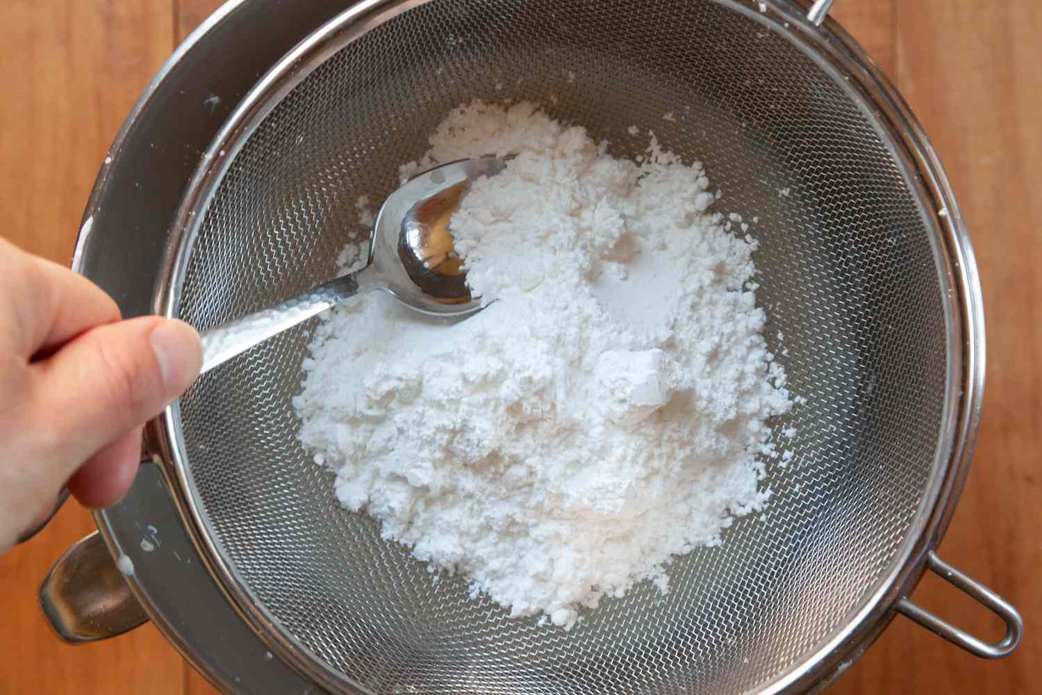Sifting powdered sugar into a stand mixer bowl to make a whipped cream frosting with cream cheese.