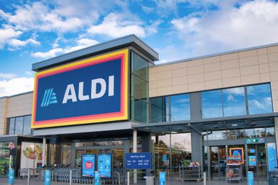 The exterior entrance of an Aldi supermarket with signage and glass windows, located under a bright sky