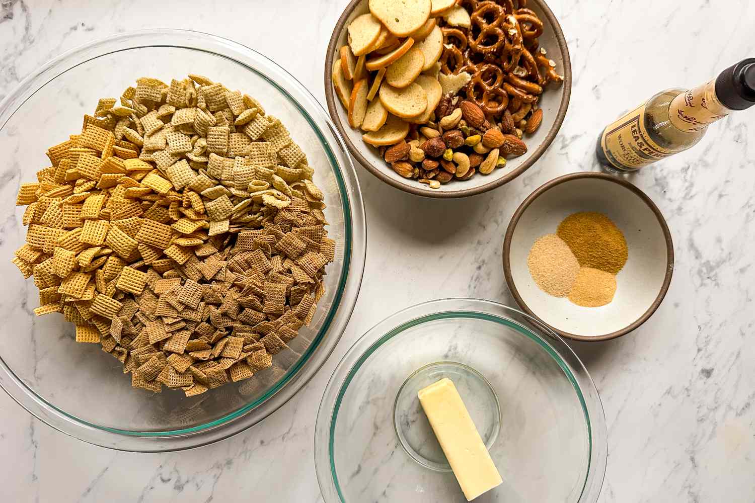 Ingredients for chex mix including cereal pretzels nuts spices butter and Worcestershire sauce on a countertop