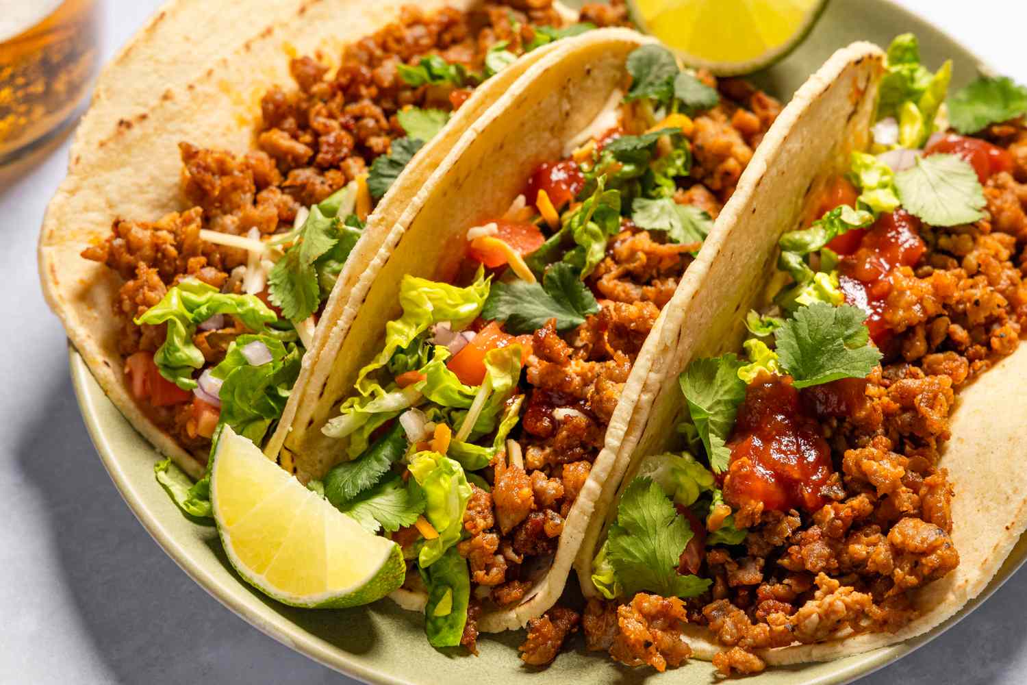 Three ground meat tacos on tortillas with lettuce and lime wedges, served on a plate