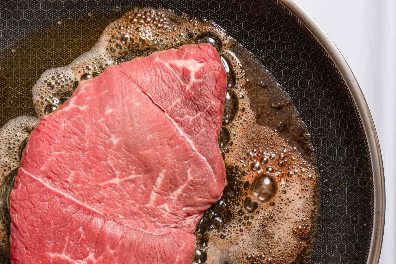 A piece of steak cooking in a frying pan