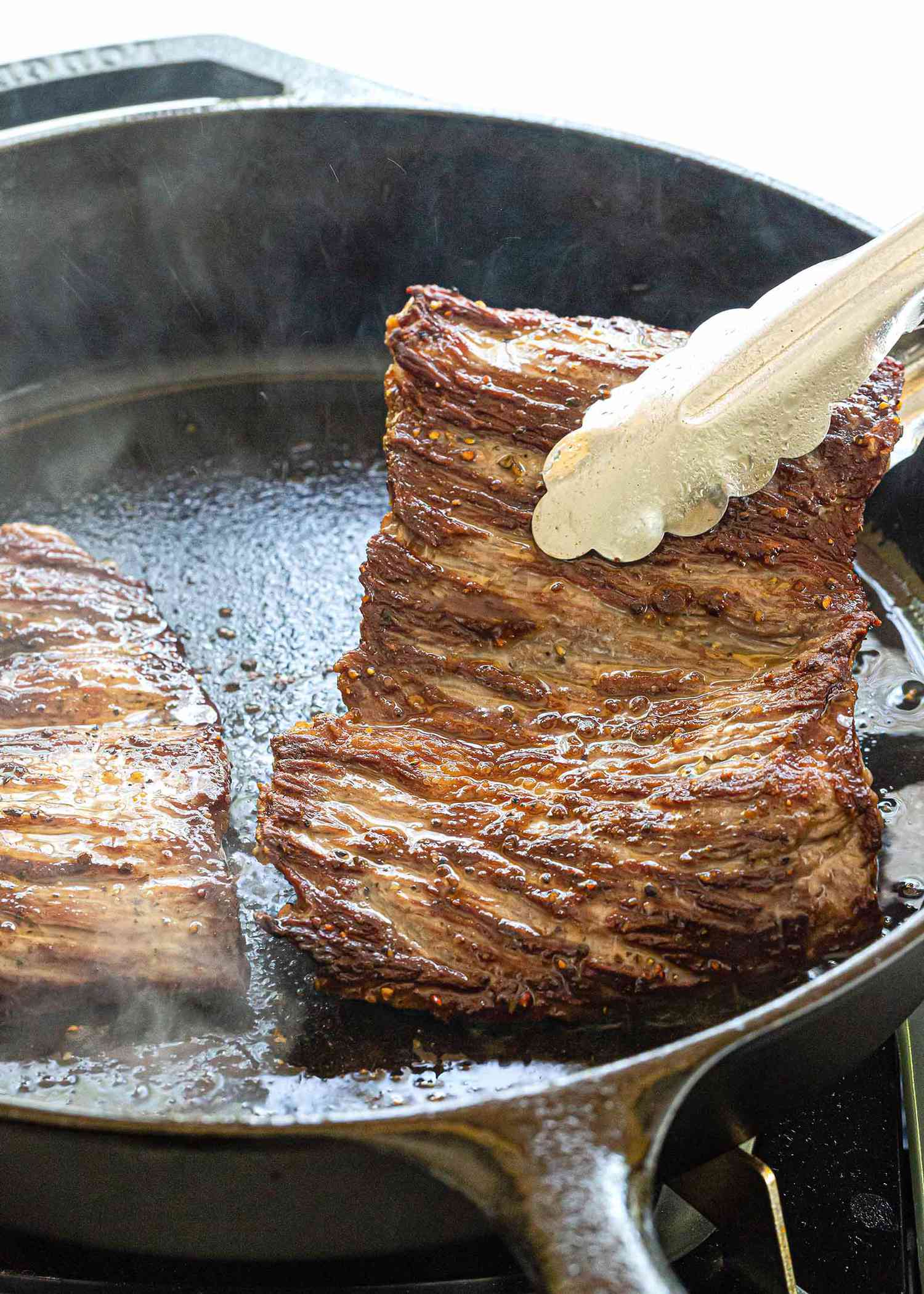 Cast Iron Skillet Skirt Steak Recipe - steak in skillet being lifted with tongs