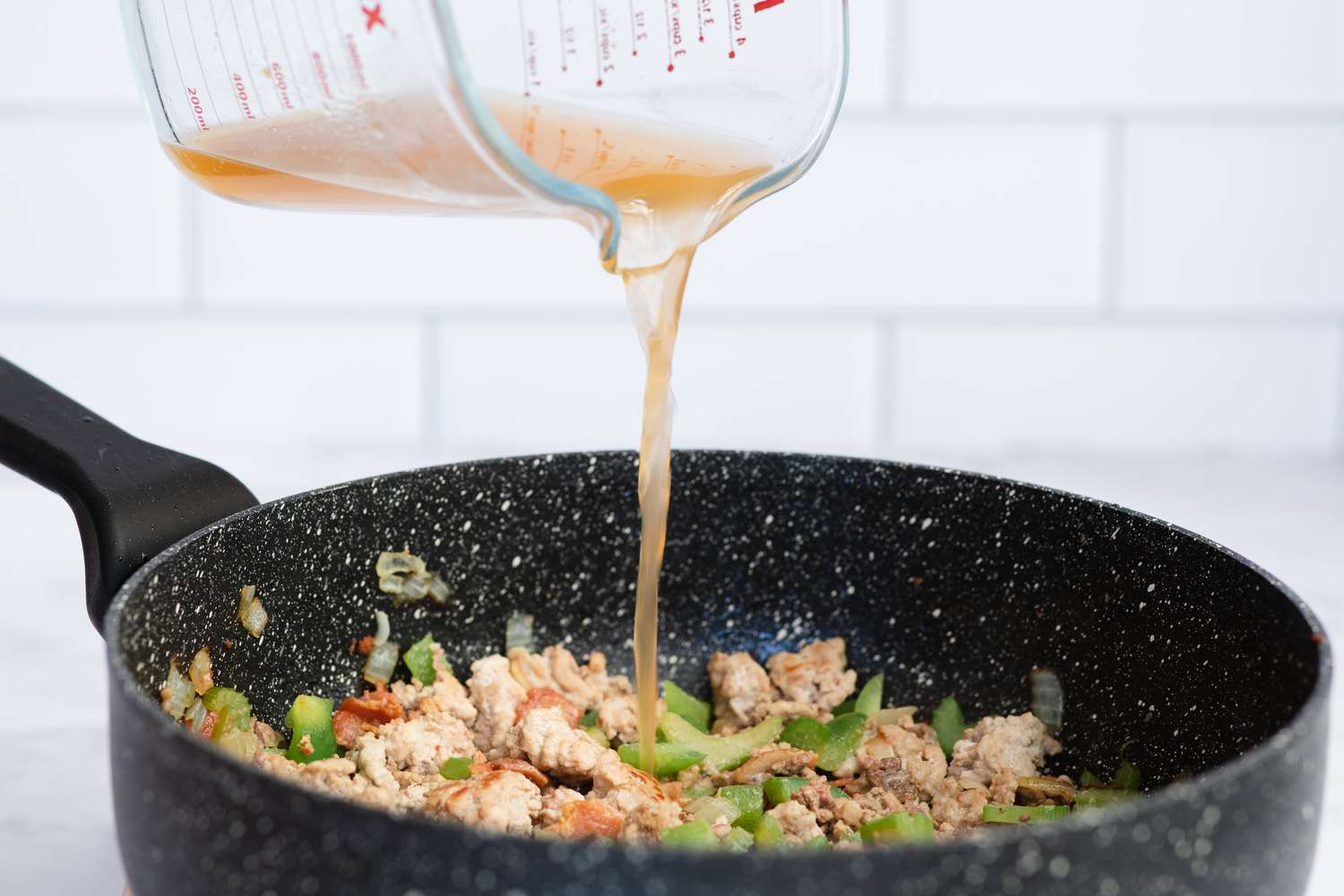 Adding broth to a skillet to make dirty rice.
