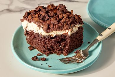 A slice of chocolate cake with cream topping and chocolate pieces on a plate with a fork