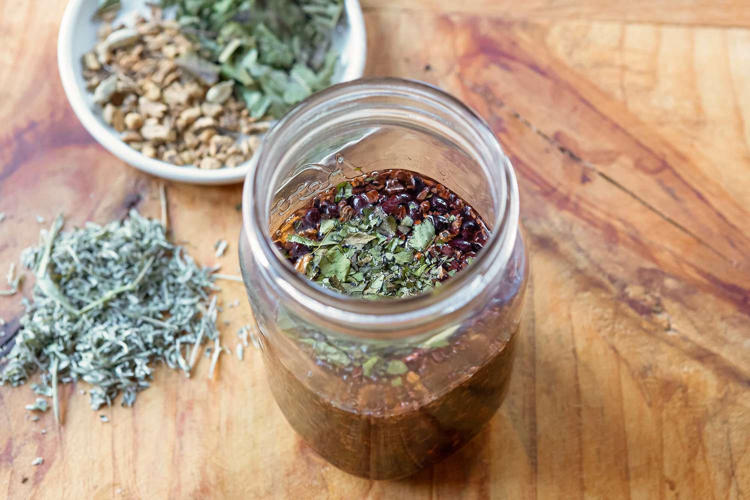 A mason jar with herbs and roots for homemade bitters.