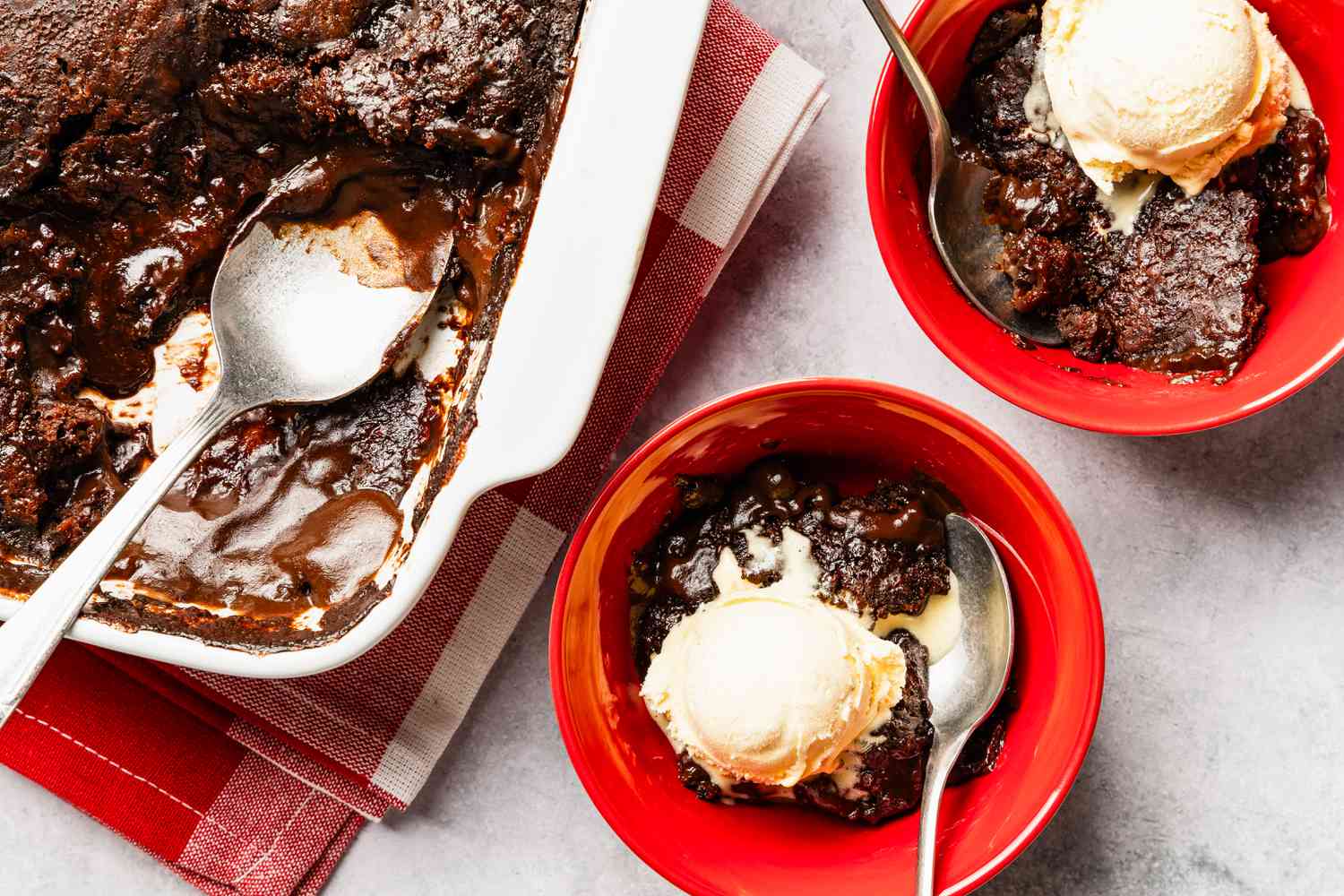 two bowls of chocolate pudding cake with scoops of vanilla ice cream next to a baking pan with more cake