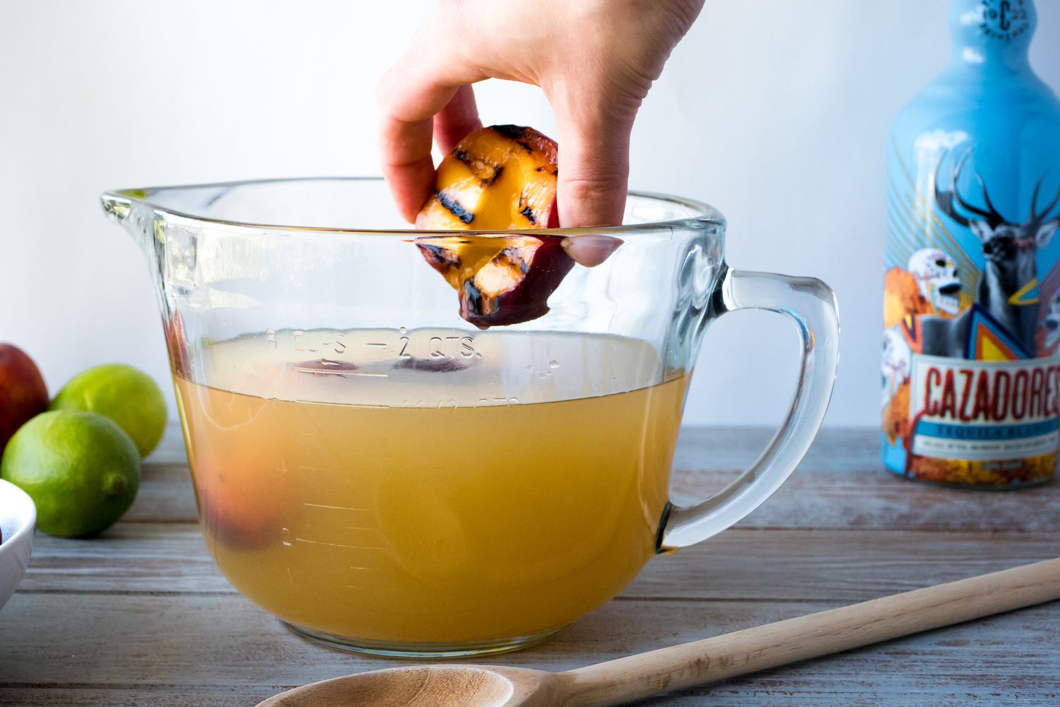 Adding grilled peaches to a glass mixing bowl to make margaritas.
