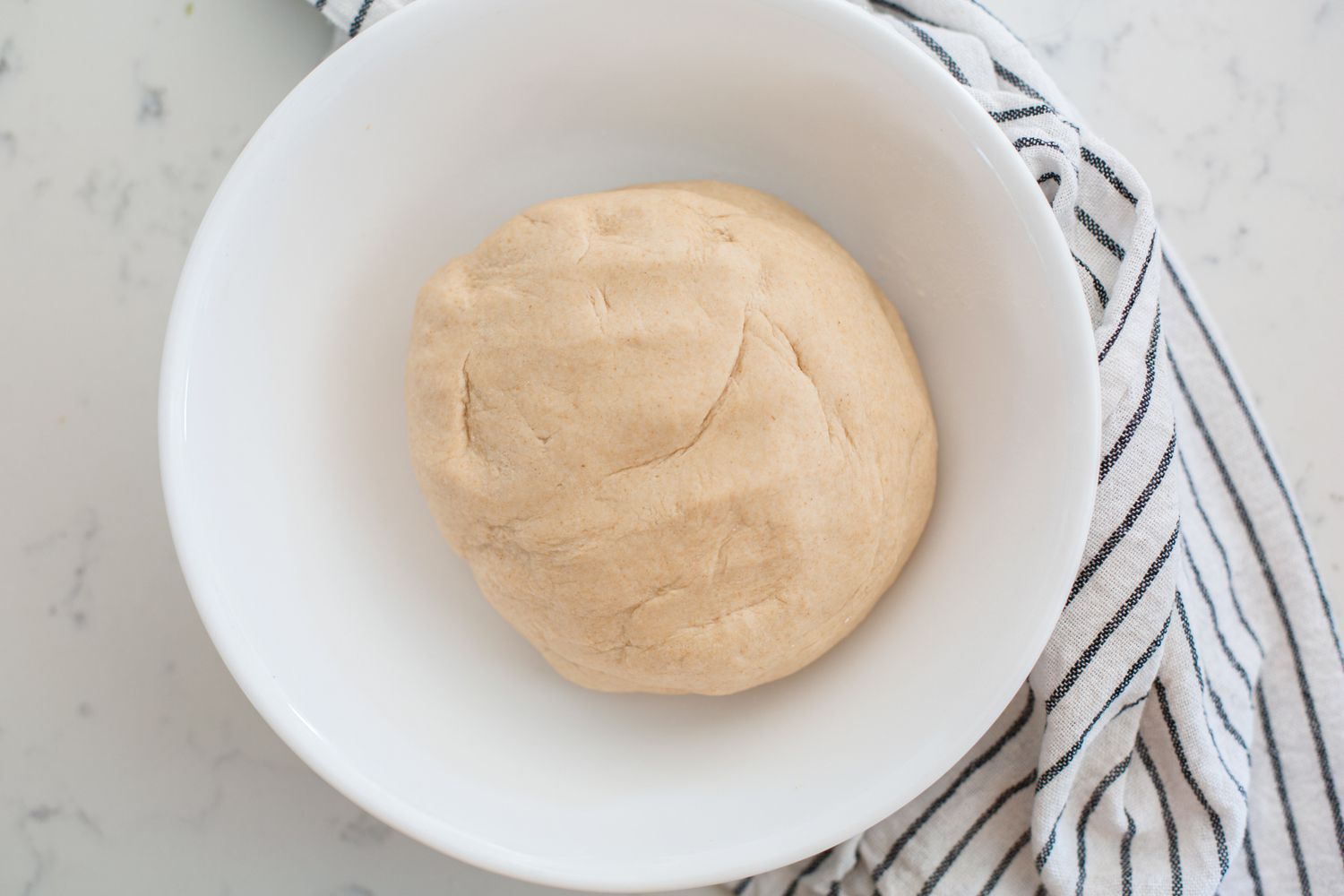 Dough to make roti in a large white bowl.