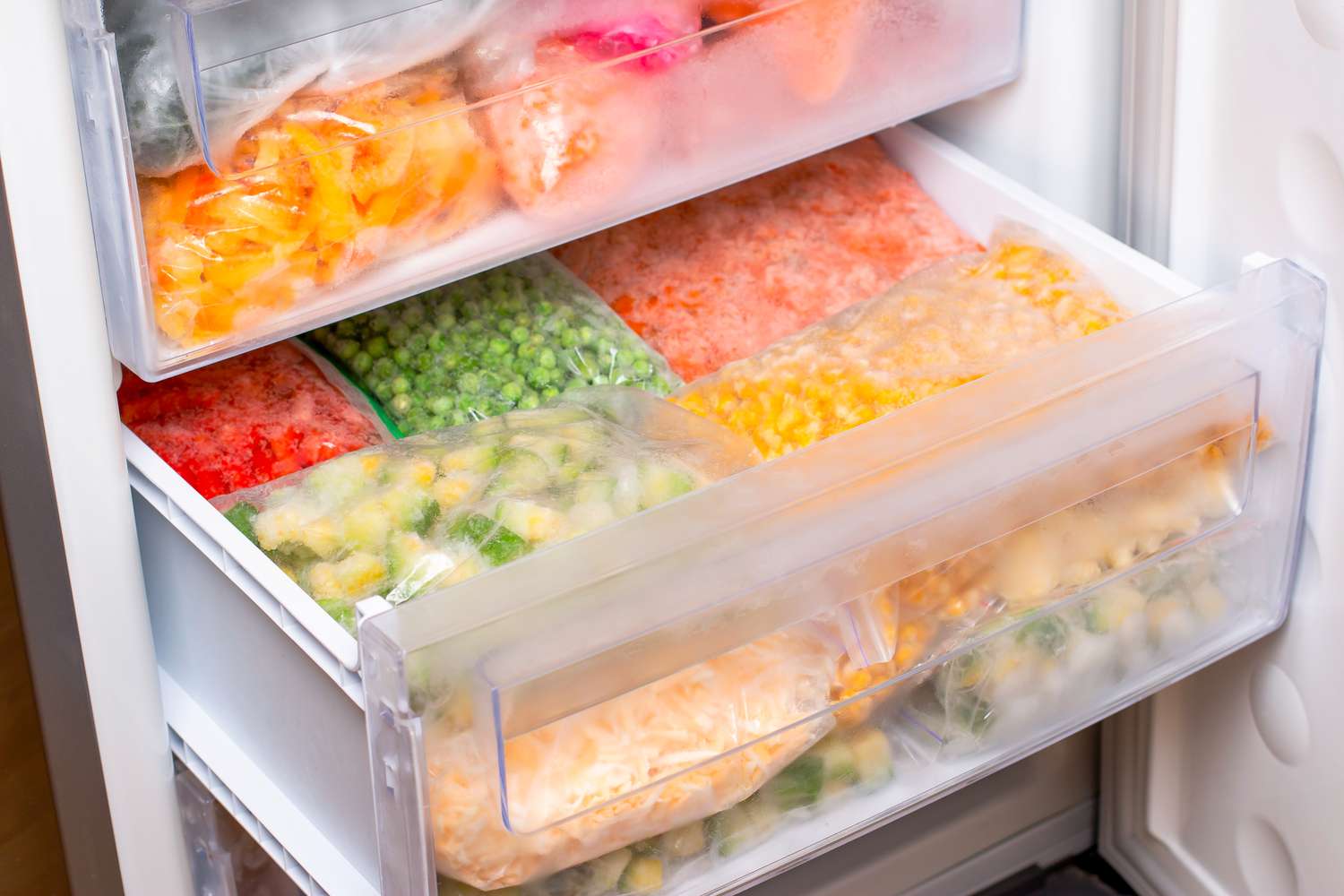 Plastic bags with different frozen vegetables in open refrigerator drawer