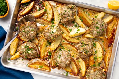 Baked meat patties and potato wedges on a tray garnished with herbs and seasoned