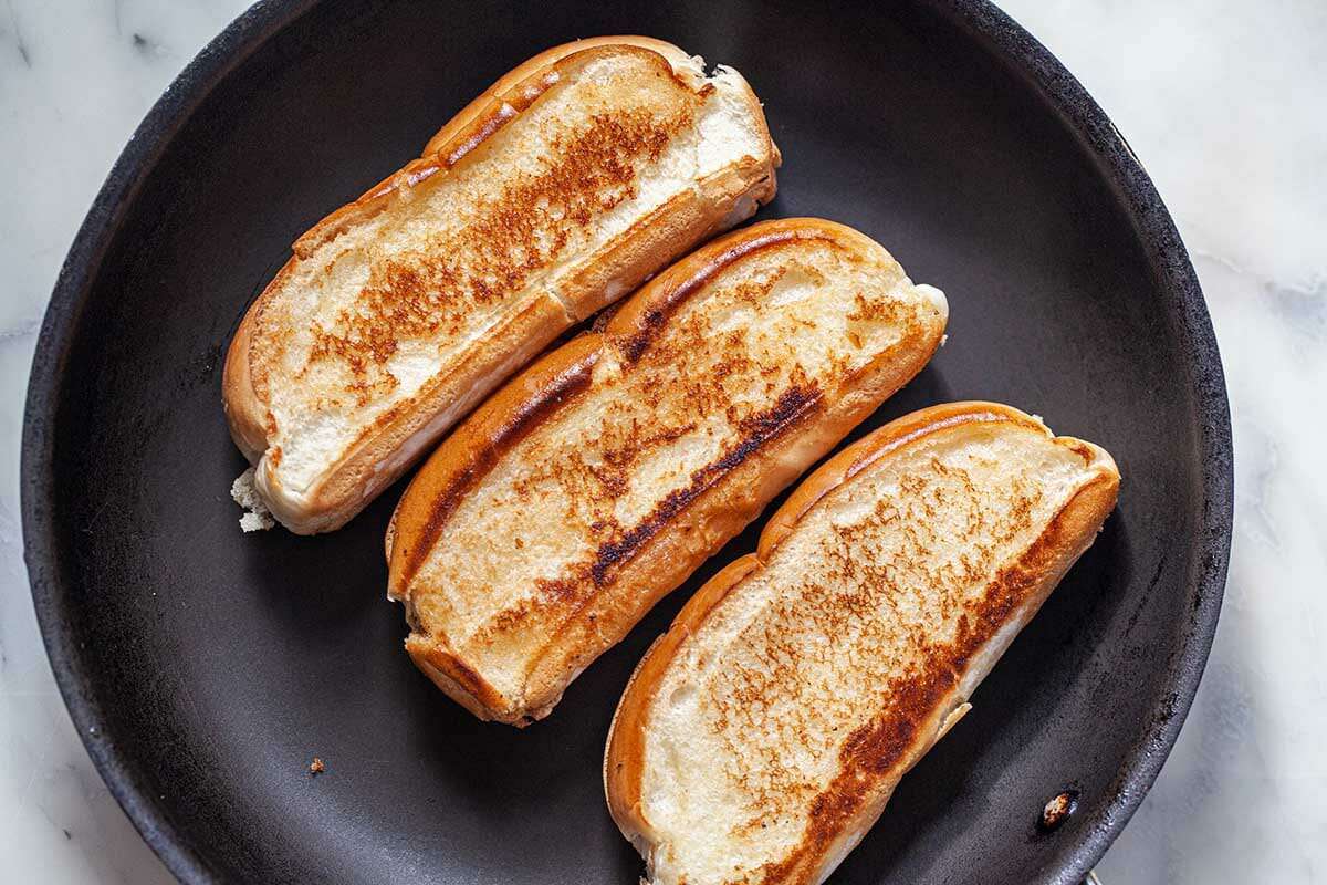 How to make lobster rolls by toasting the bun. Three split buns, toasted and on a plate.