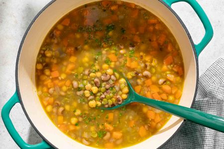 A pot of threepea soup with a ladle containing visible peas carrots and herbs