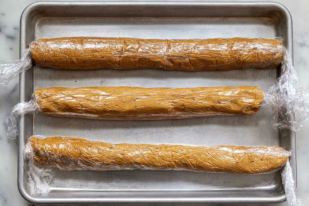 Three logs of dough wrapped in plastic wrap and set on a baking sheet to make Easy Ginger Lemon Cookies.