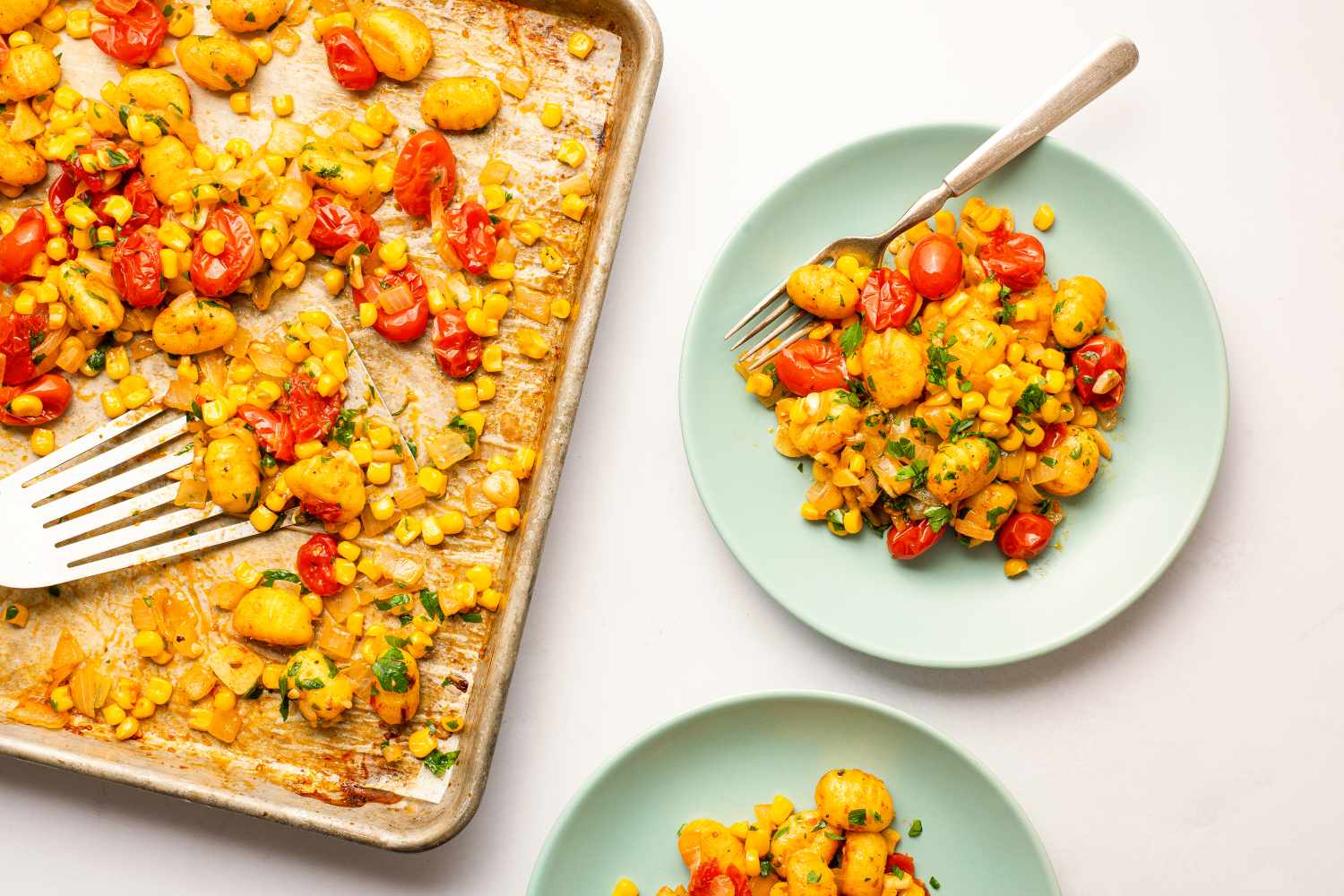 Sheet pan of baked gnocchi with corn and tomatoes, plates with servings of the dish