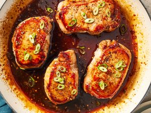 Cooked pork chops garnished with sliced green onions in a pan of sauce
