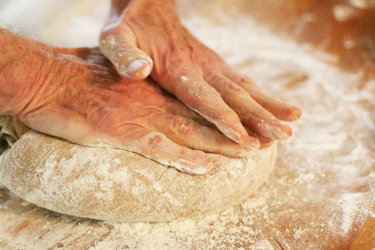 Two hands pressing down and shaping rye bread dough