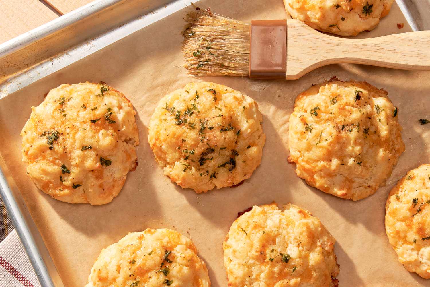 Copycat Red Lobster cheddar bay biscuits on a baking sheet with a pastry brush 