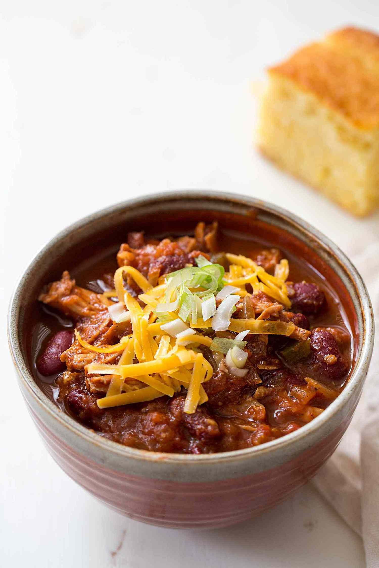 A bowl of turkey chili ready to eat, with cornbread in the back
