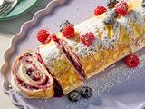 Rolled crepe cake with berry filling dusted with powdered sugar and garnished with fresh raspberries and blueberries on a platter