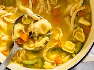 A pot of chicken tortellini soup with vegetables with a ladle scooping a serving