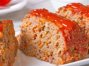 Slices of meatloaf topped with a layer of red sauce arranged on a plate