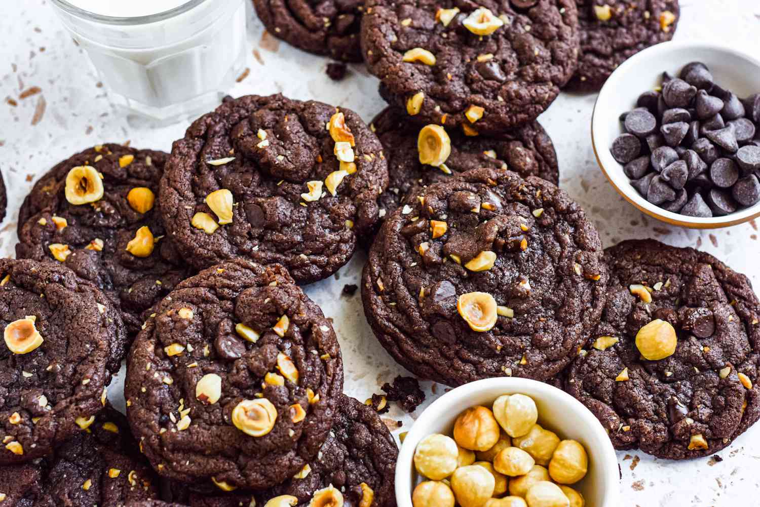 Overhead view of nutella cookies and hazelnuts scattered on a white surface.