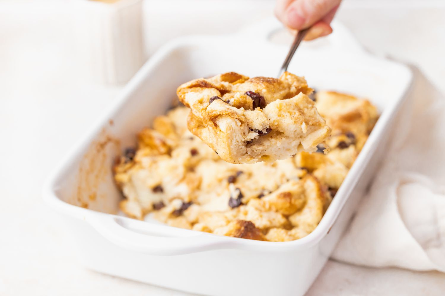 A spoonful of easy bread pudding taken out of a white casserole dish.