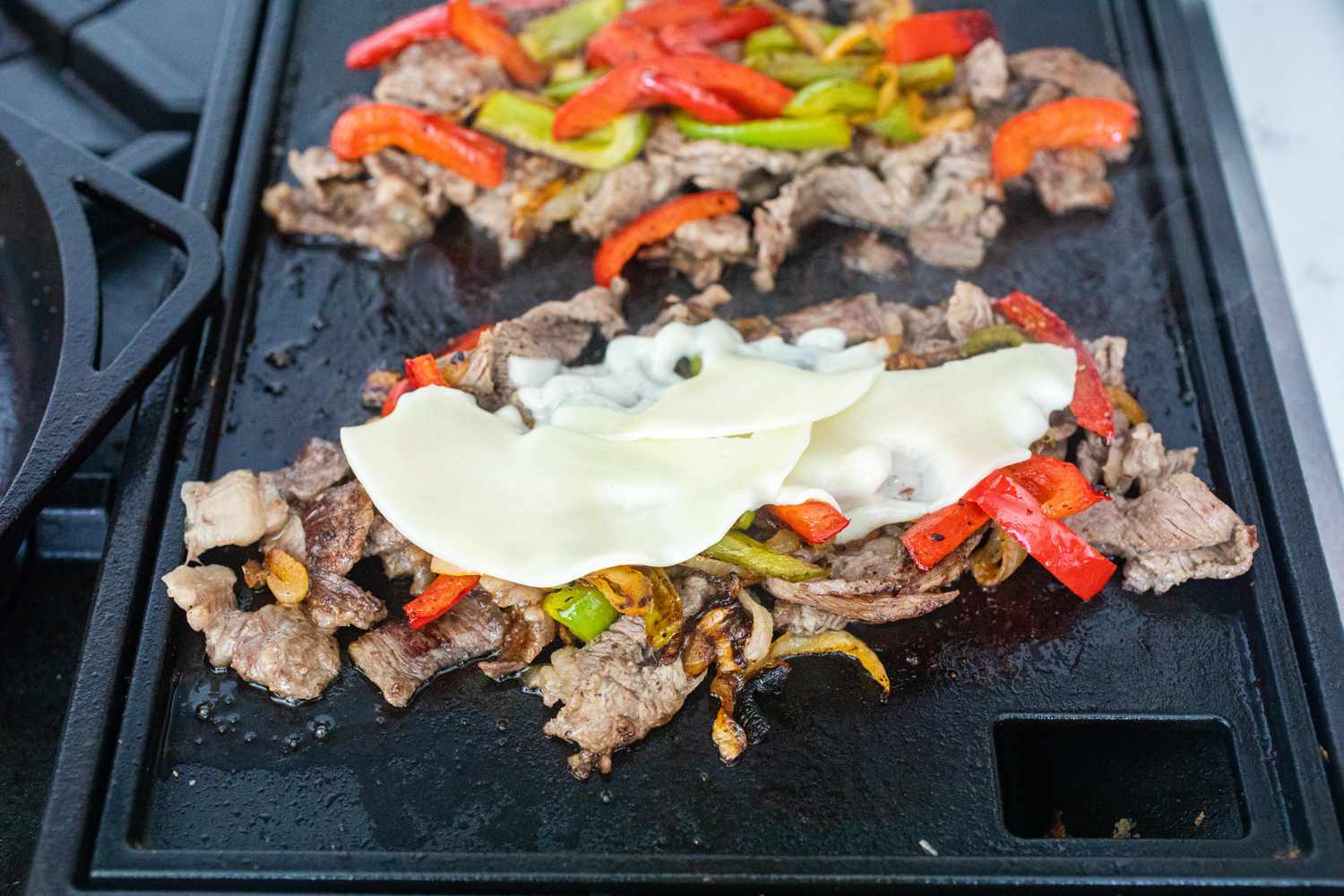 Beef and peppers topped with cheese and on a griddle to make an authentic Philly cheesesteak recipe.