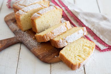 Slices of A slice of Olive Oil Yogurt Cake on a wooden paddle and dusted with powdered sugar.