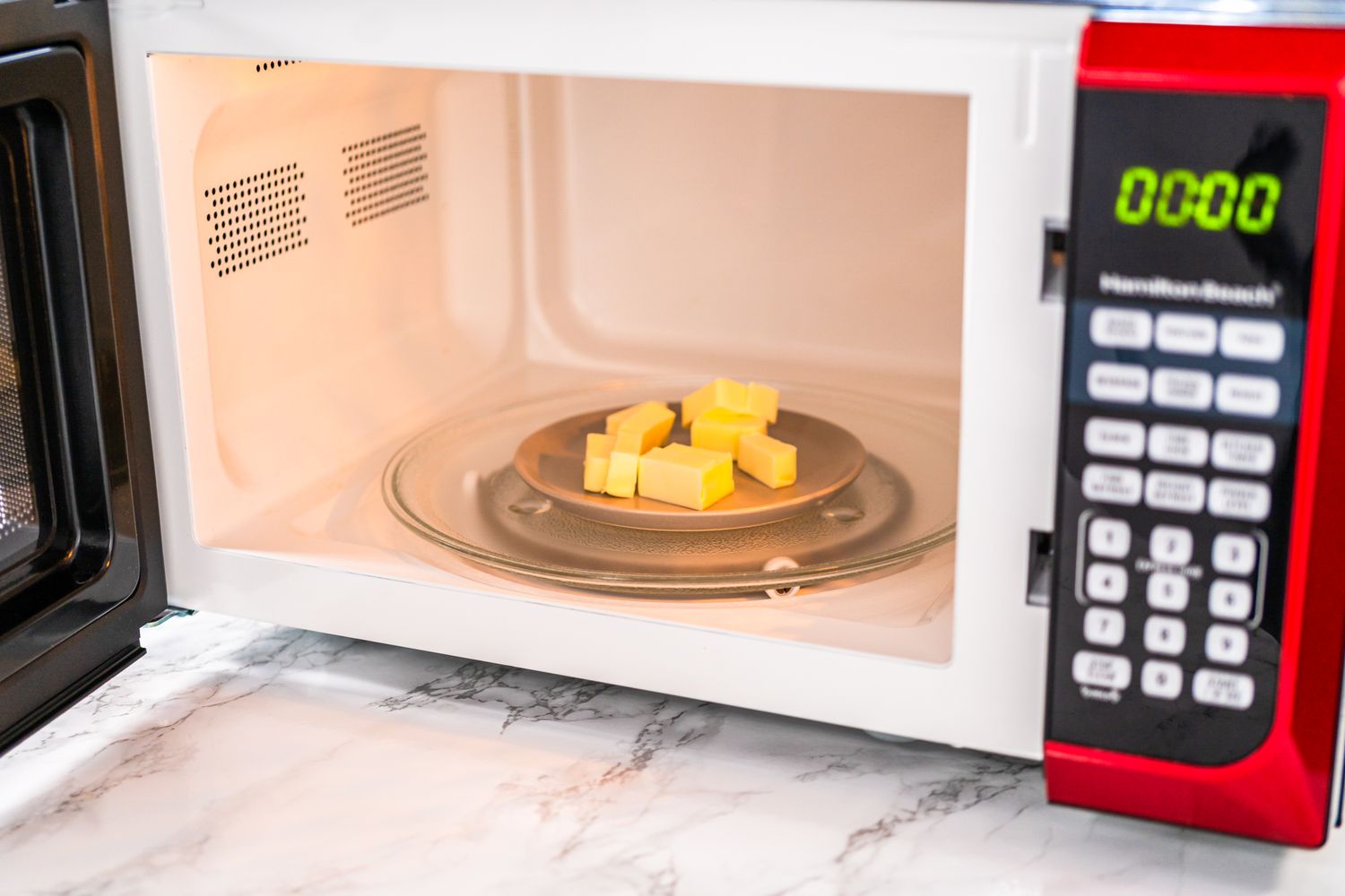 Butter cubes on a plate in a microwave oven with a marble countertop visible