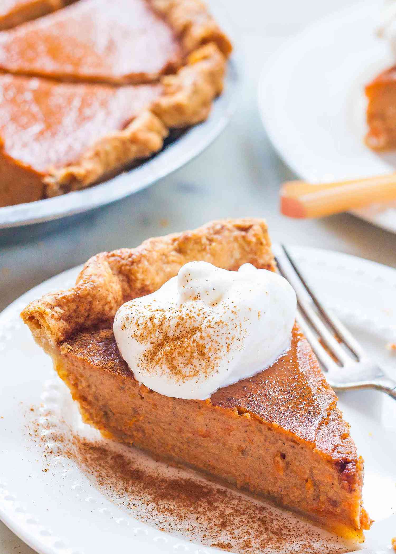 Slice of sweet potato pie on a white plate with whipped cream dusted with cinnamon and fork.
