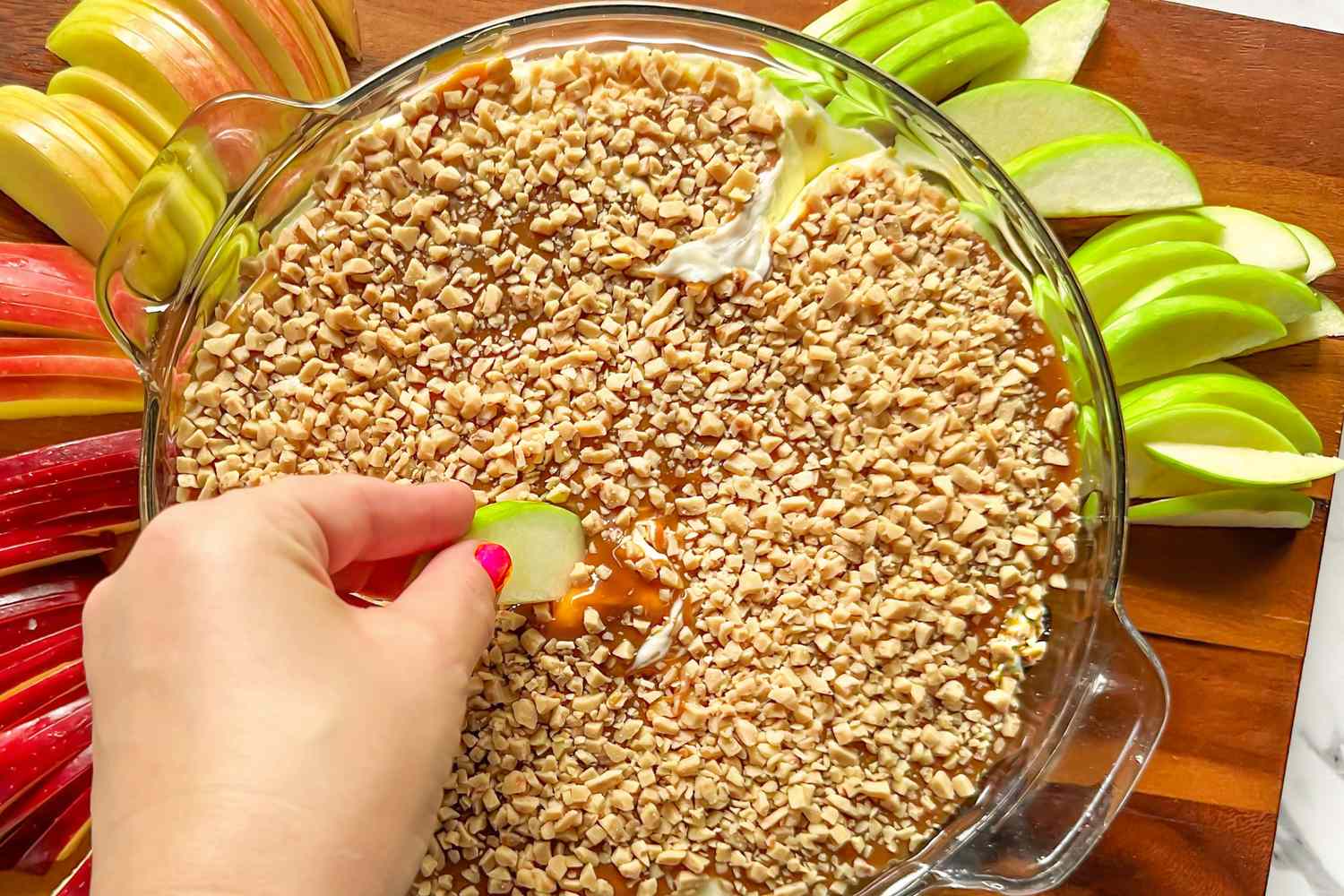 Hand scooping caramel apple dip with sliced apple