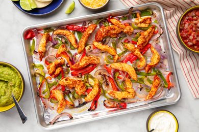 Sheet pan with cooked chicken strips and assorted vegetables surrounded by small bowls of guacamole pico de gallo and condiments