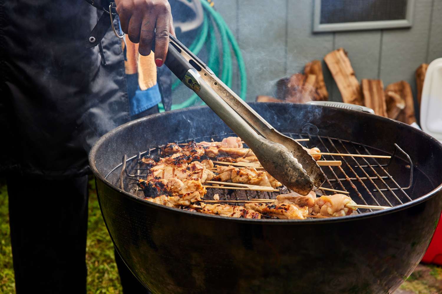 Grilling chicken skewers on a barbecue grill using tongs, outdoor setting with cooking in progress