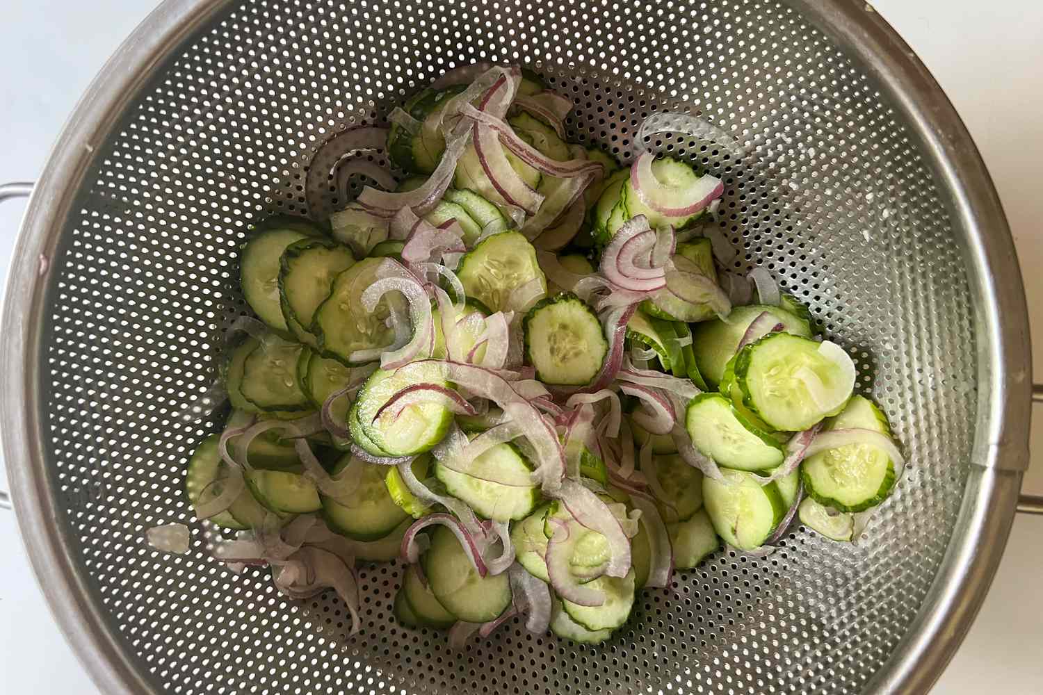 Sliced cucumbers and onions in a colander