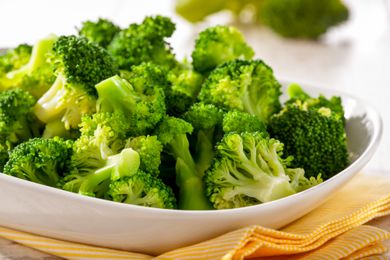 Closeup of a white bowl of steamed broccoli on top of a yellow cloth napkin