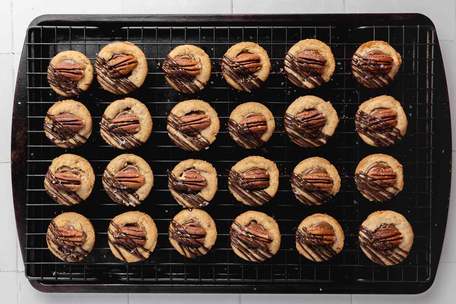 Chocolate Drizzle Added to Turtle Cookie Cup Resting on a Wire Rack over a Baking Sheet Pan