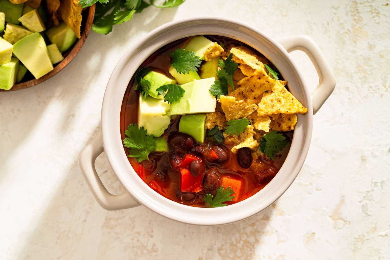 Bowl of tortilla soup with avocados chips and cilantro garnishes