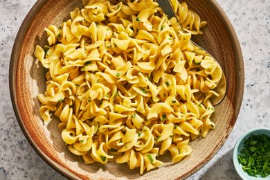 A bowl of buttered noodles garnished with herbs with a small dish of garnishes on the side