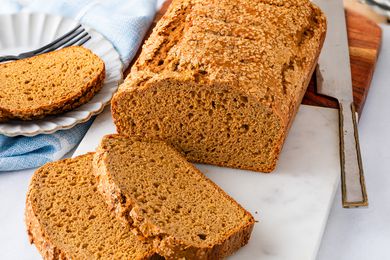 Angled view of a loaf of pumpkin bread on a marble cutting board with two slices in front and one on a plate to the side