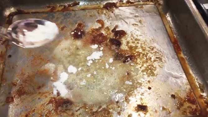 Flour being spooned over the drippings in a baking sheet