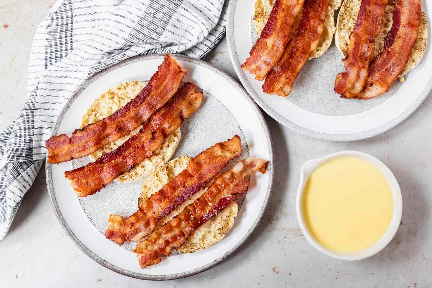 English muffins topped with bacon with hollandaise sauce on the side