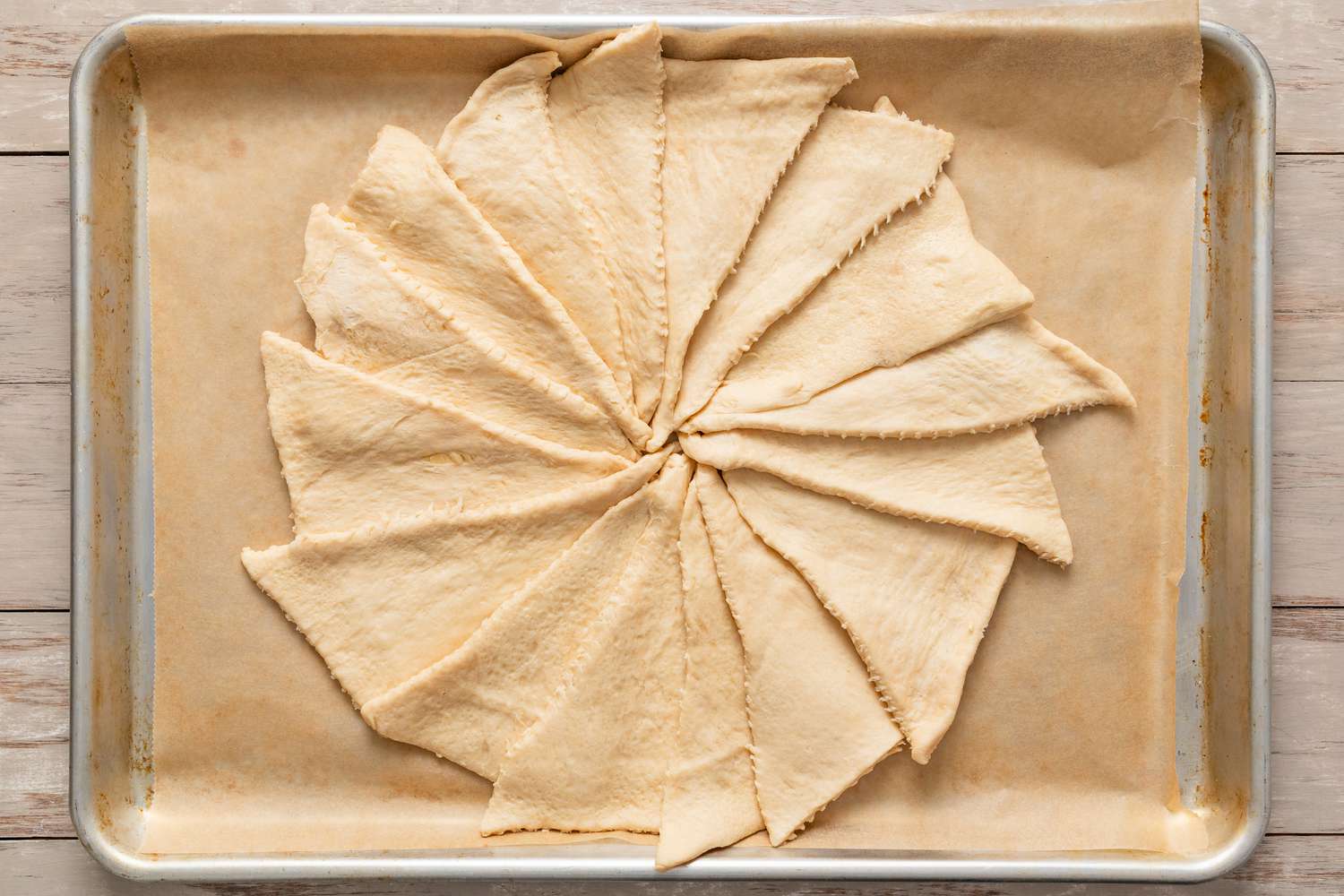 Crescent dough triangles arranged in a circle on a parchment paper lined baking tray for mardi gras king cake recipe