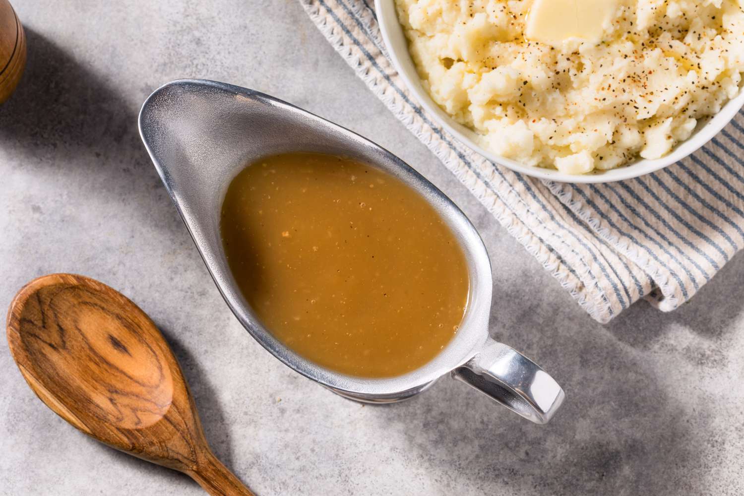 Brown turkey gravy in a b, next to a bowl of mashed potatoes and a wooden serving spoonoat