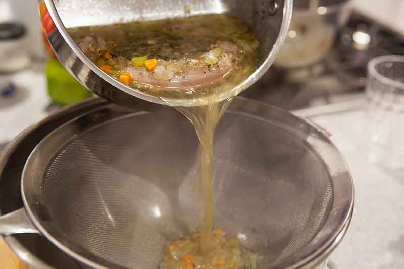 Giblet mixture being poured into a strainer to remove the solid pieces 
