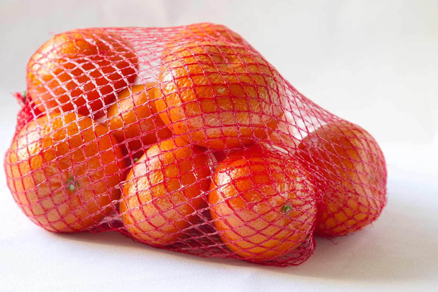 Oranges in a red mesh bag on a white background