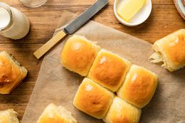 Milk Bread Rolls on a Piece of Parchment Paper with Some Rolls Torn Off, Surrounded by a Glass of Milk and a Saucer with Butter