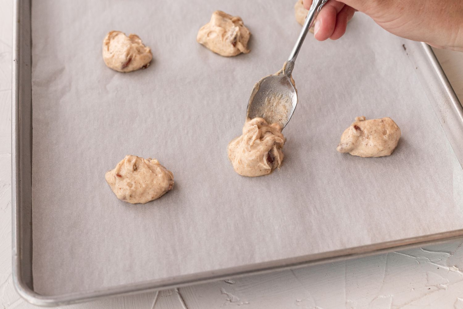Dropping banana cookie dough onto a parchment lined baking sheet.