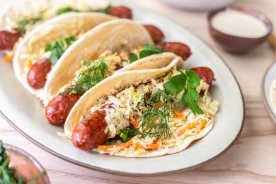 Plate of Ronto Wraps Topped With Herbs, Slaw, and Dressing, and in the Background, a Bowl of Coleslaw, a Plate With Pita Bread, and a Bowl of Dressing